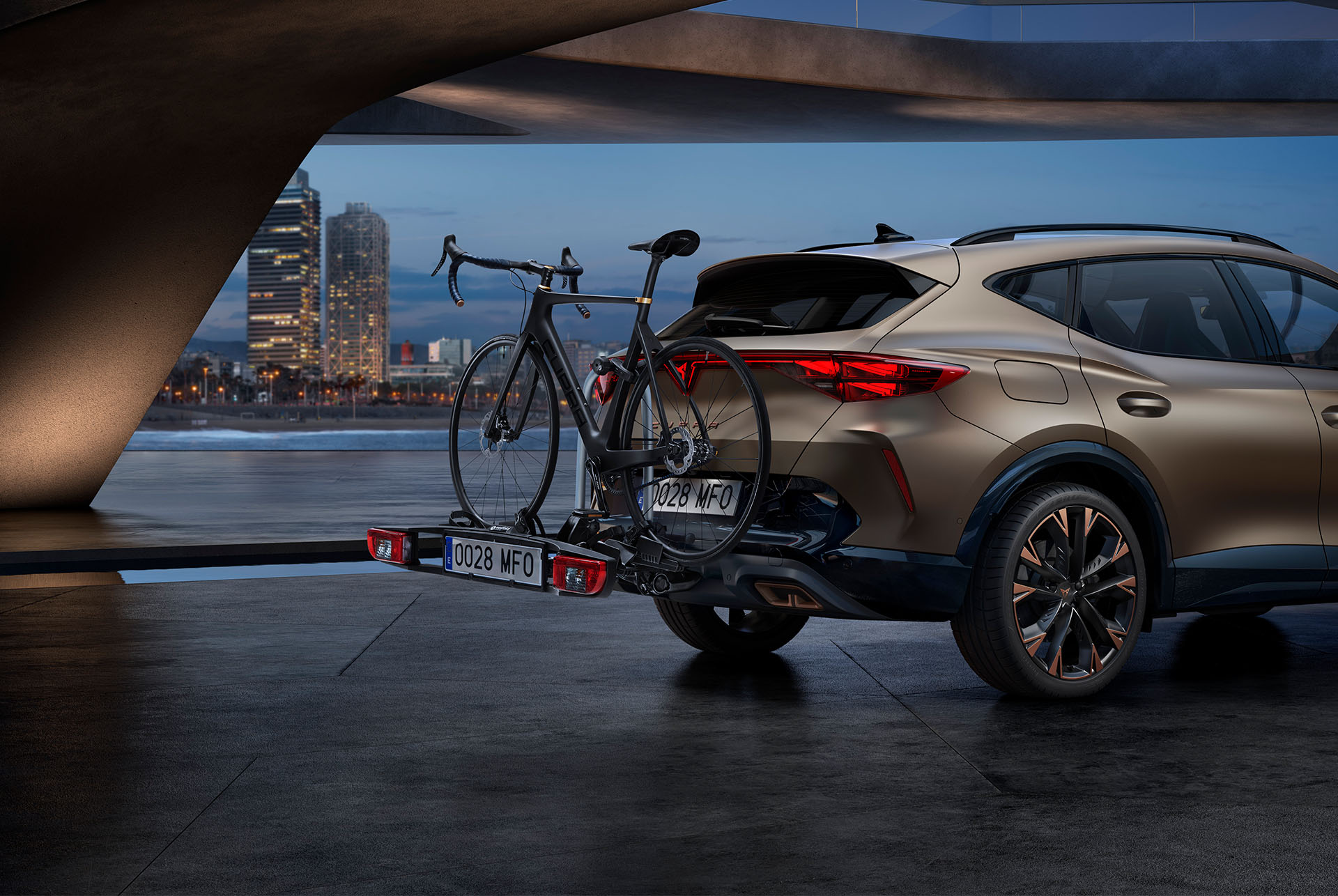 Nouveau CUPRA Formentor 2024 en Century Bronze, porte-vélos sur attelage de remorque, la ville en arrière-plan.