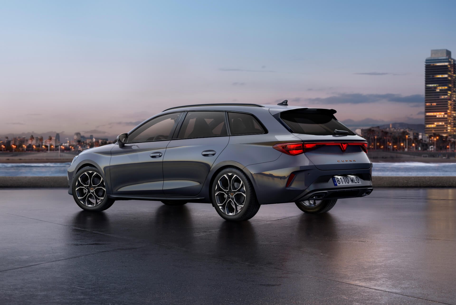 Vue arrière du nouveau modèle Cupra Leon Sportstourer 2024 en Gris Brillant avec réglage adaptatif du châssis et jantes en alliage noir et cuivre. Ville en arrière-plan au coucher du soleil.