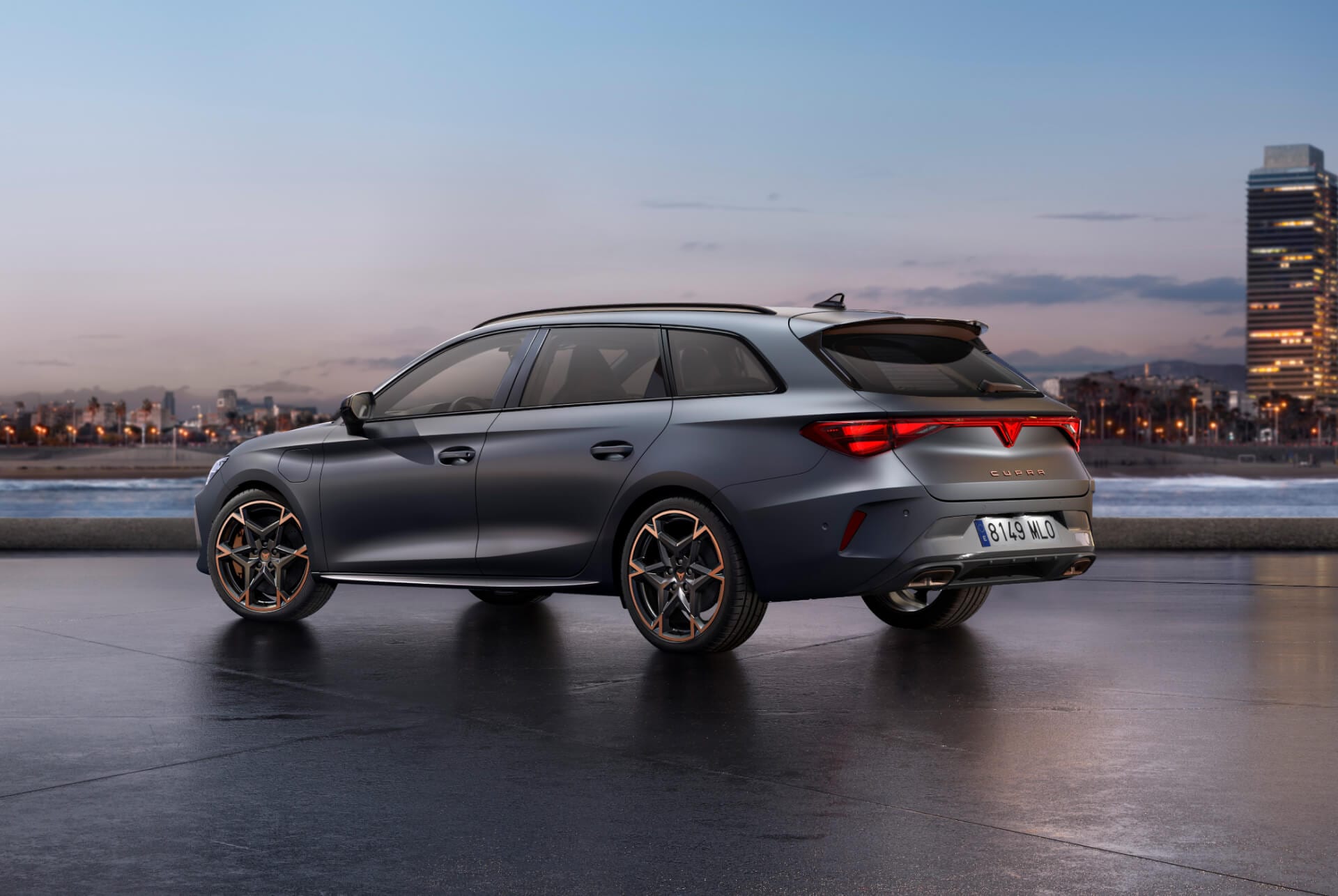 La nouvelle Cupra Leon Sportstourer 2024 sportive est garée sur du béton avec, en arrière-plan, la ligne d’horizon de la ville illuminée au crépuscule. Le véhicule est représenté dans une finition gris mat.