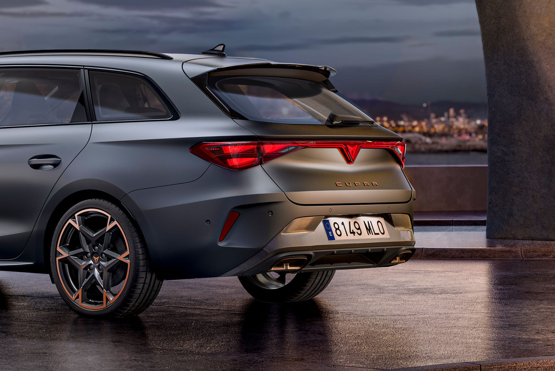 Gros plan de la vue latérale arrière de la nouvelle voiture hybride Cupra Leon 2024 en Gris Encelade mat, jantes forgées aux accents cuivrés, structure en béton et la ville à l’horizon