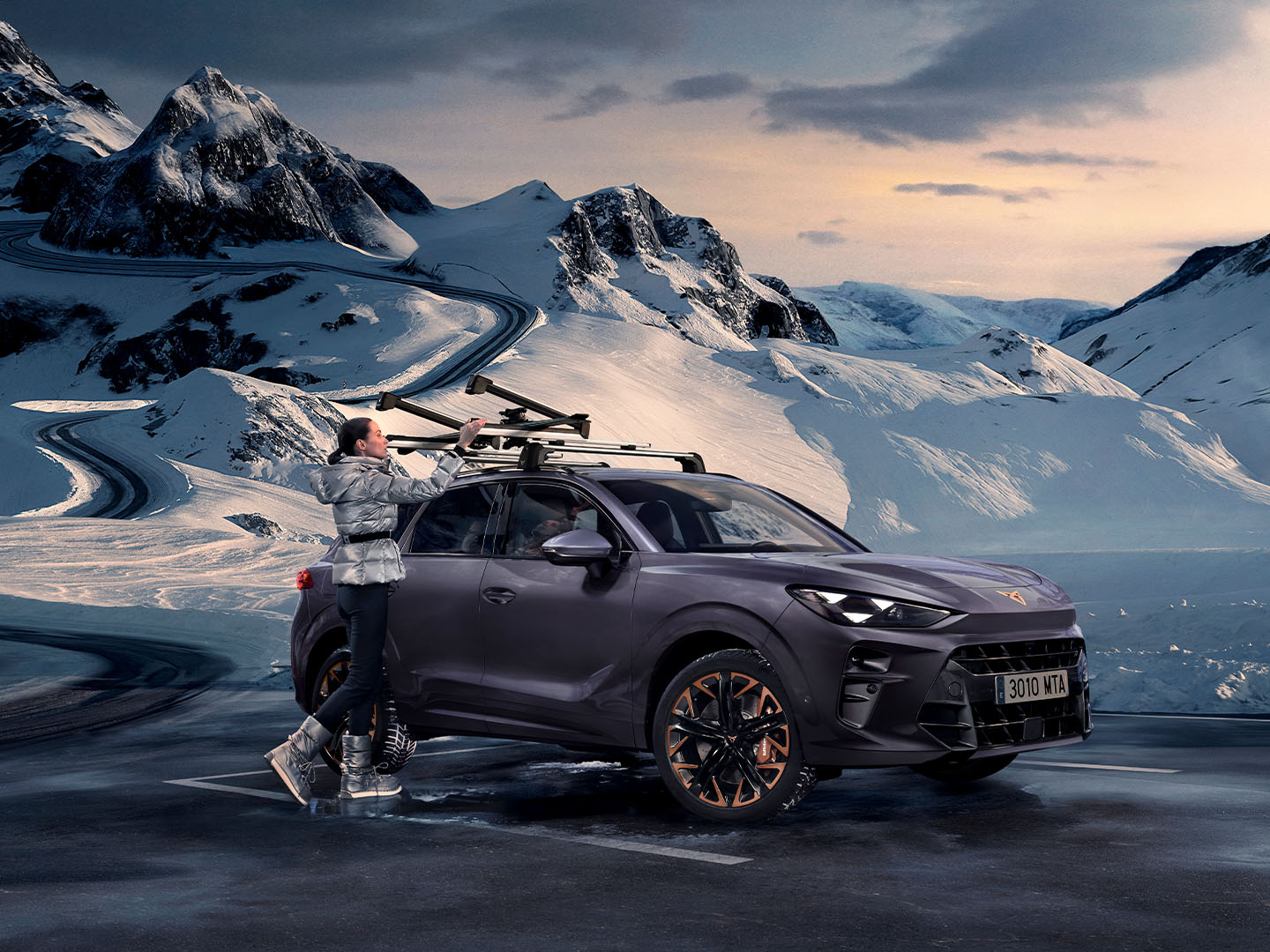 CUPRA Terramar dans un décor enneigé, présentant le porte-skis, l’un de ses accessoires de transport, monté sur le toit. Une femme utilise ce porte-skis pour transporter ses skis