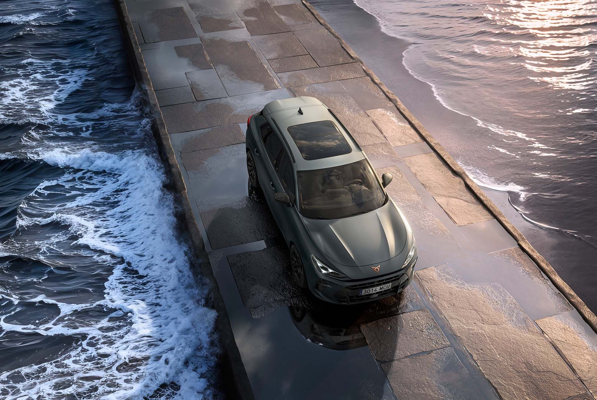 nouveau modèle suv hybride cupra terramar 2024 doté d’un toit ouvrant panoramique, d’un design épuré et de jantes en alliage modernes sur une chaussée mouillée en bord de mer, vue du dessus.
