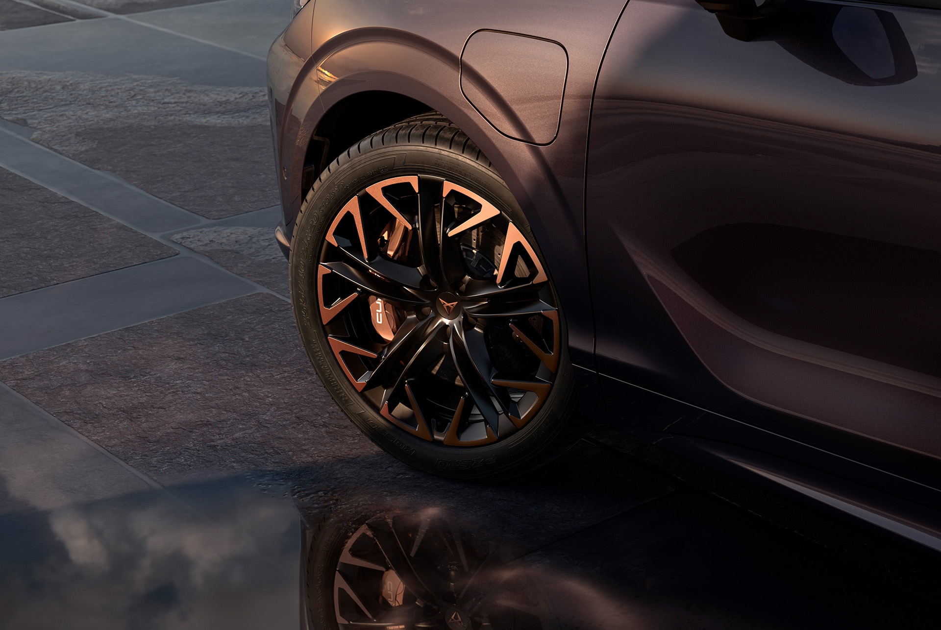 Jante en alliage cuivre hadron 20 pouces sur le nouveau cupra terramar, en noir avec des accents cuivrés. L’arrière-plan dépeint une chaussée pavée. On y voit également une partie de la carrosserie brillante et sombre de la voiture.