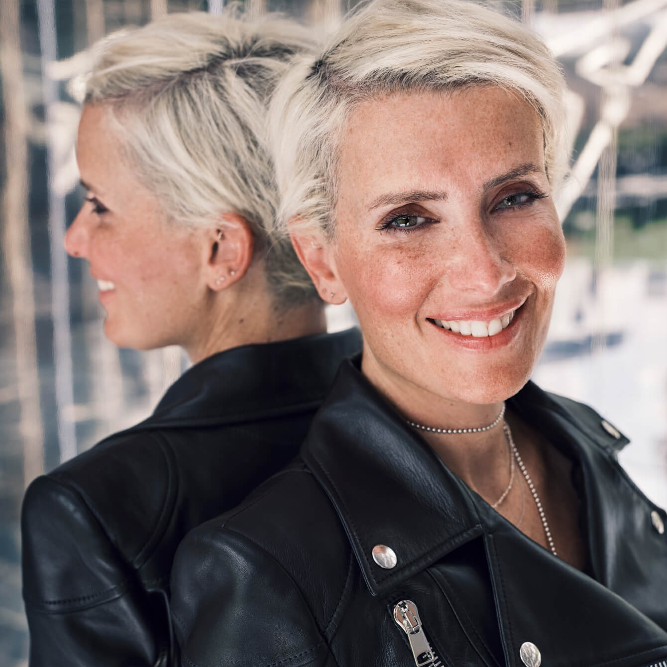 Cecilia Taieb, appuyée contre le miroir, souriante, avec une veste en cuir noire.