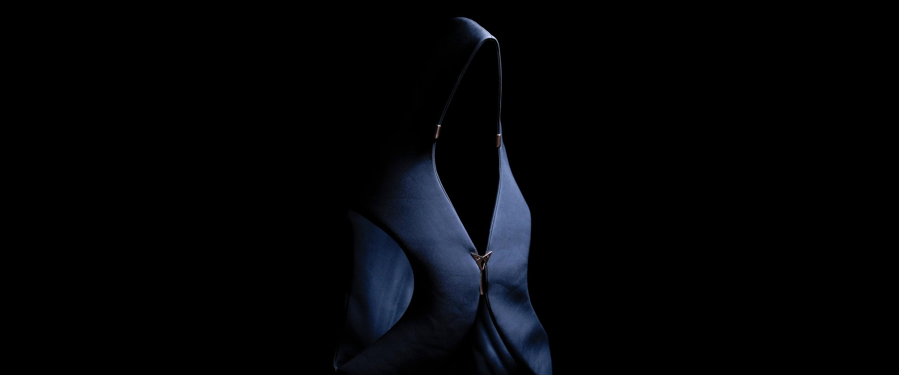 Un vêtement foncé à capuche, doté d’une fermeture éclair apparente, est éclairé de manière saisissante sur un fond noir, créant une image de mode abstraite et mystérieuse.