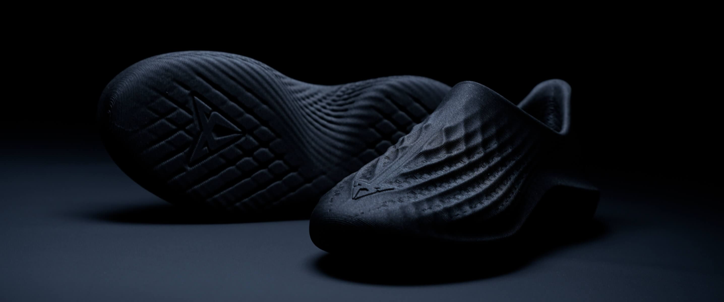 Une paire de chaussures foncées et texturées présentée dans une photo de produit sur fond sombre.