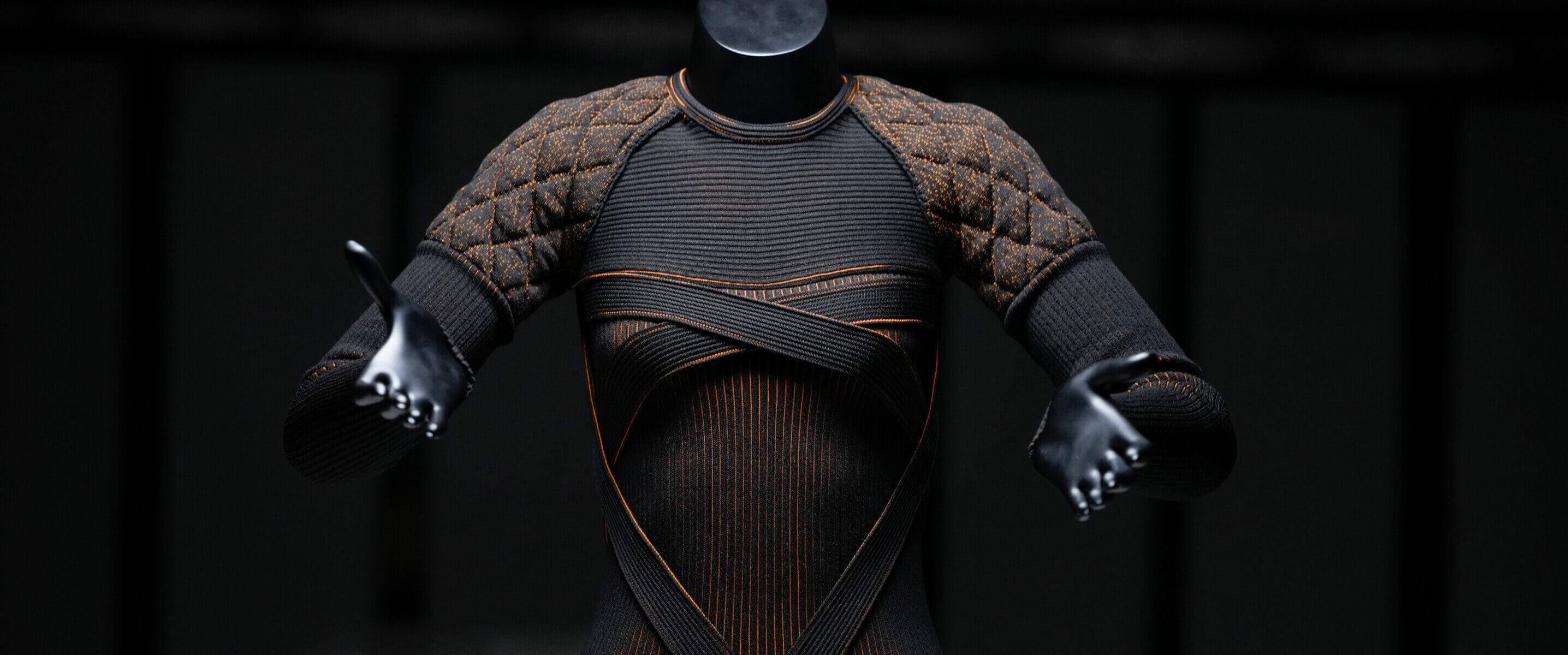 Un haut texturé présenté sur un mannequin noir sur fond sombre, posé sur une surface blanche.