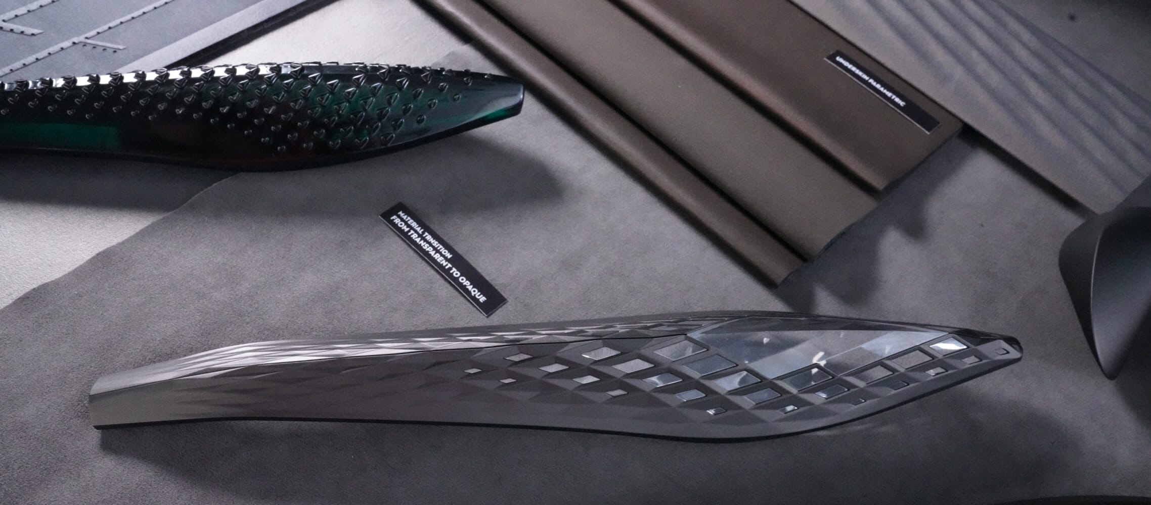 Des pièces de design automobile de couleur grise, gris foncé et vert foncé sont exposées sur une surface grise.