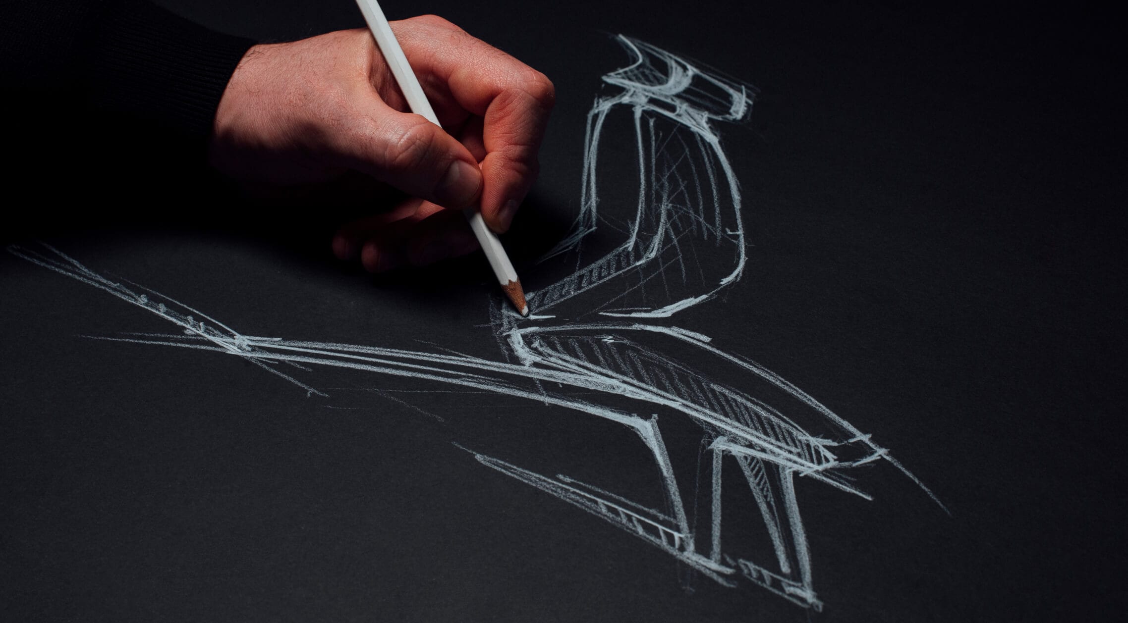 Une main tenant un crayon blanc dessine l’esquisse d’une chaise avec des lignes blanches sur du papier noir.