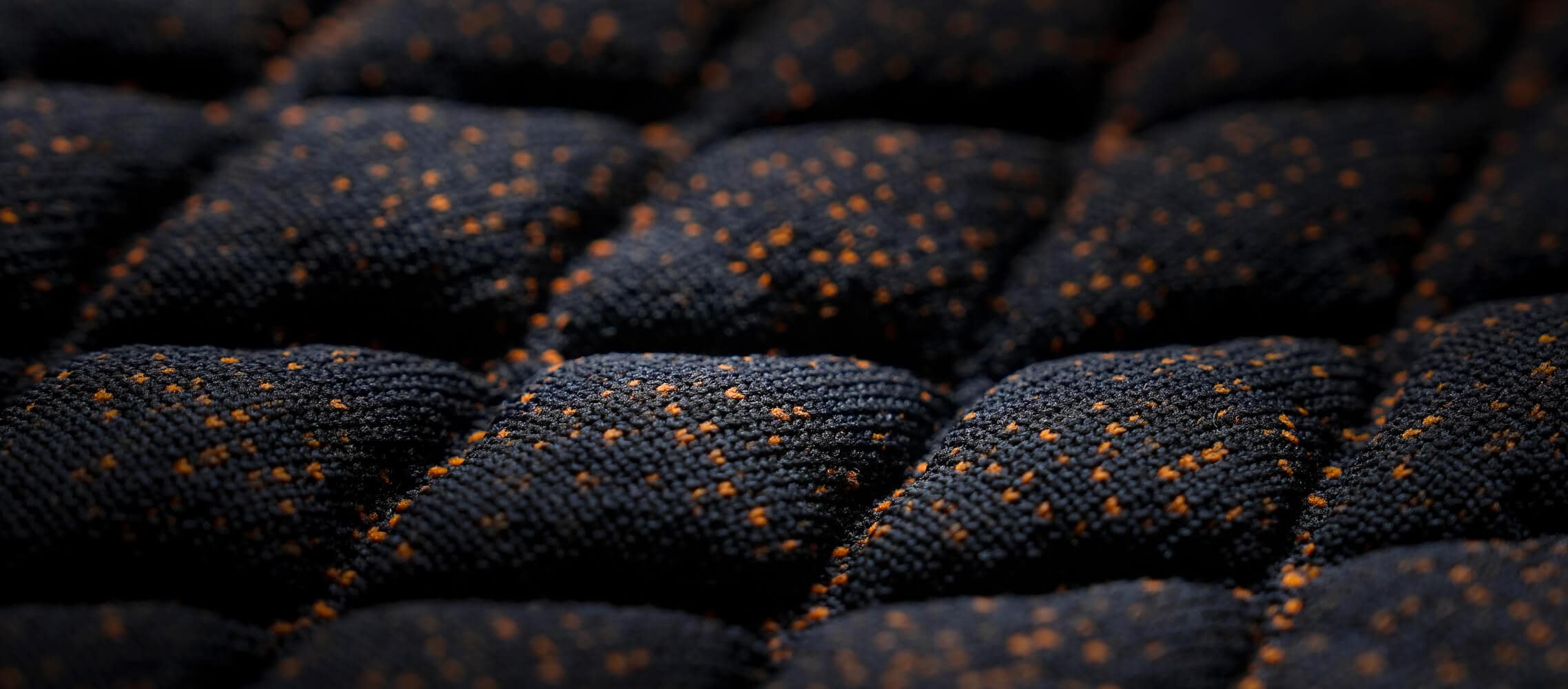 Gros plan d’un tissu matelassé foncé avec un motif en losange en relief et de petites touches orange. 