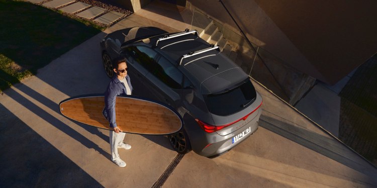 Personne avec une planche de surf s'apprêtant à la charger sur un Cupra formentor, obtenu dans le cadre d'une offre de location simple.