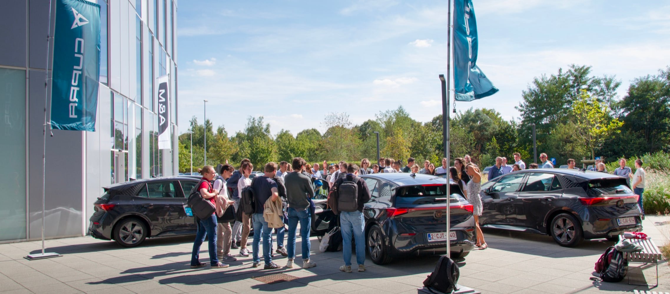 Véhicules électriques, voitures de société devant les bureaux de Cegeka, arbres et ciel bleu.