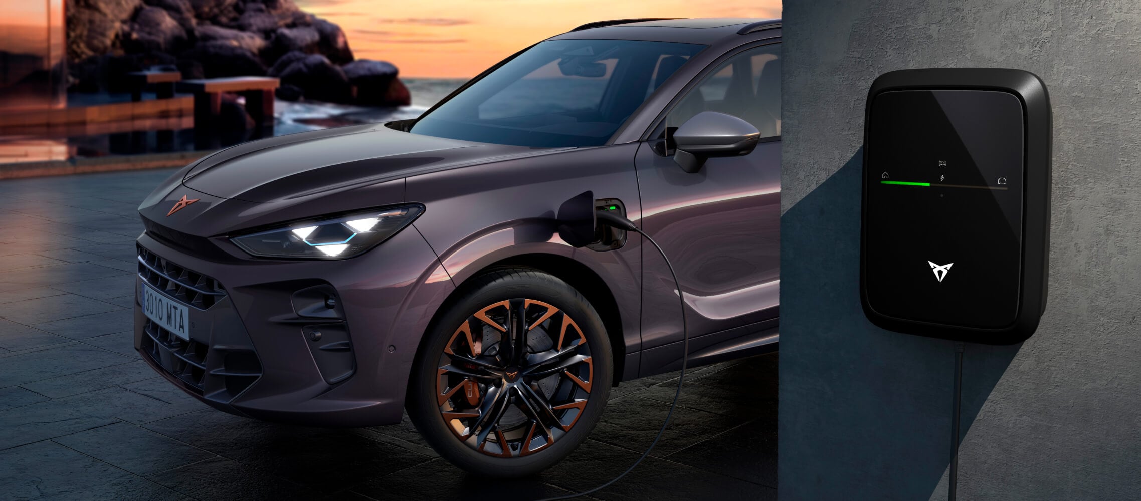 Voiture de société hybride rechargeable cupra terramar vz, pour les solutions de flotte cupra, de couleur dark void, stationnée, en train de charger avec le chargeur cupra, en arrière-plan un paysage de campagne au coucher du soleil.