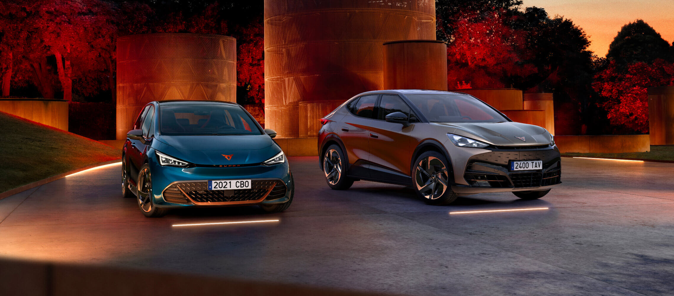 Une CUPRA Born et une CUPRA Tavascan, garées à l’extérieur, dans un parc, entourées de lumières tamisées