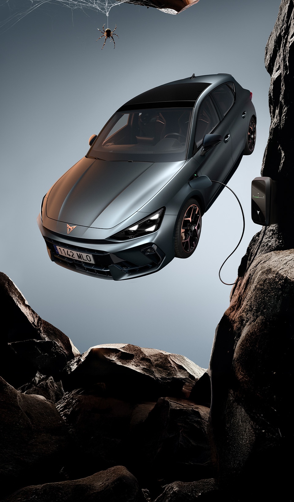 A CUPRA Formentor CUV suspended diagonally, next to a rocky, cliff-like structure. A charging cable is connected to the car from a charging unit on the cliff face.