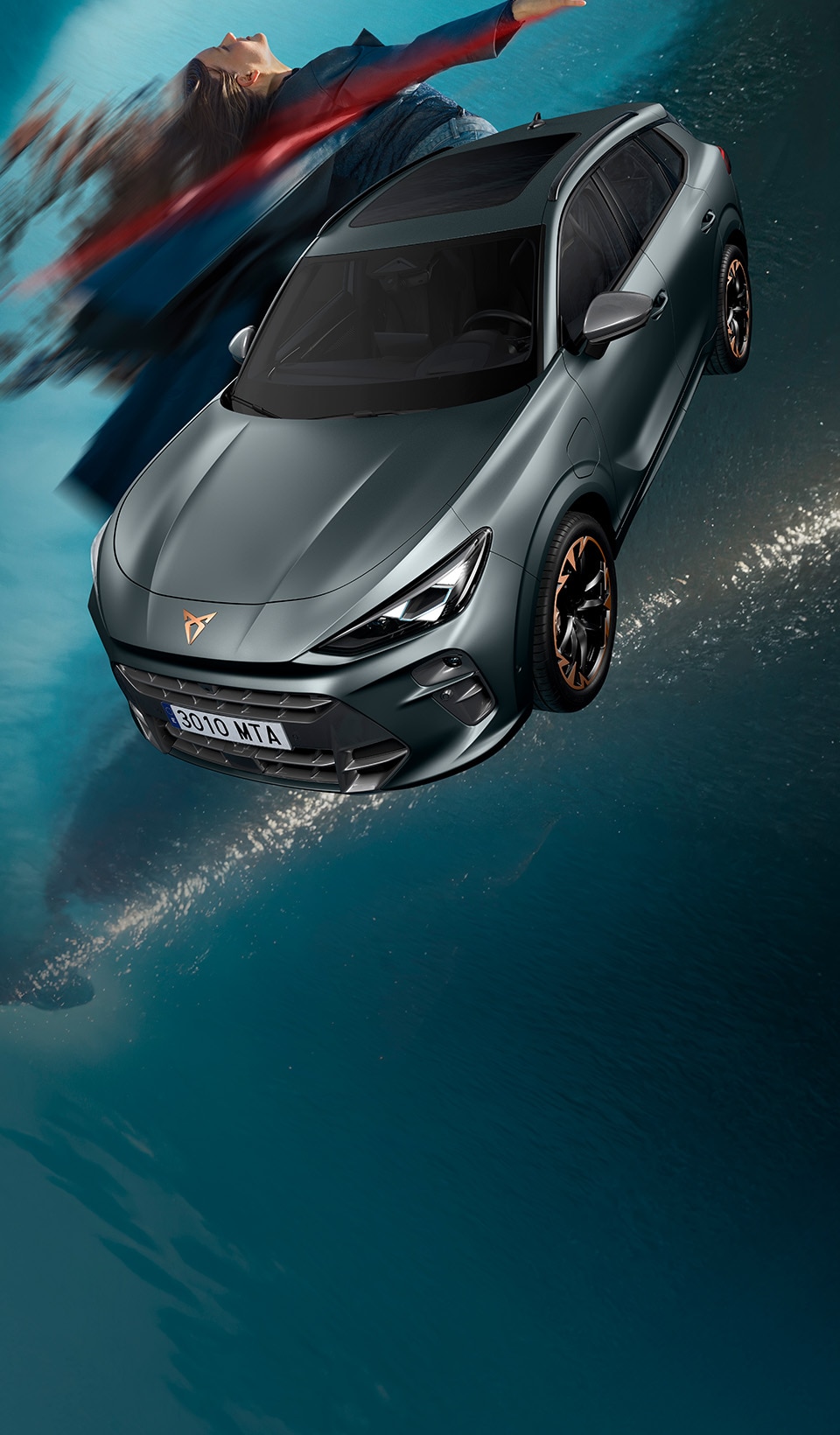 A CUPRA Leon hatchback seen from an elevated angle with its headlights on, next to a person covered in dark, flowing fabric that drapes onto the ground.